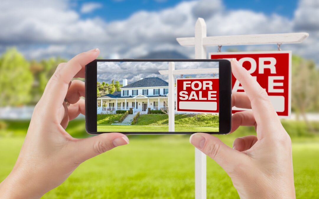 Phone photographing a house with a For Sale sign