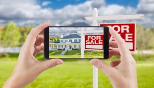 Phone photographing a house with a For Sale sign